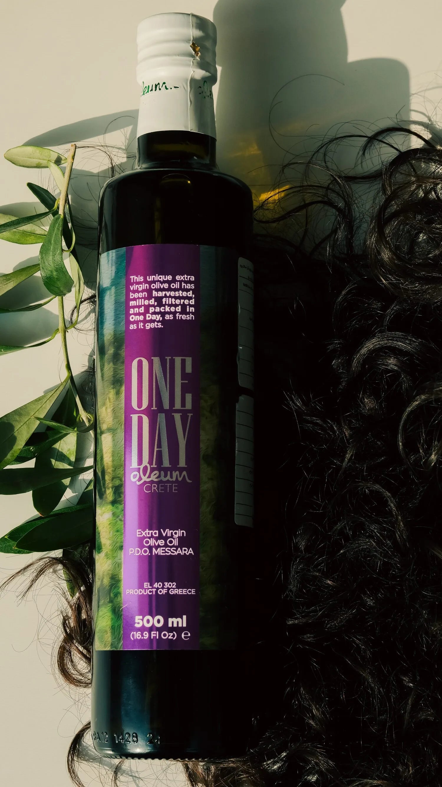 An olive-oil hair oil beside dark curls in sunlight